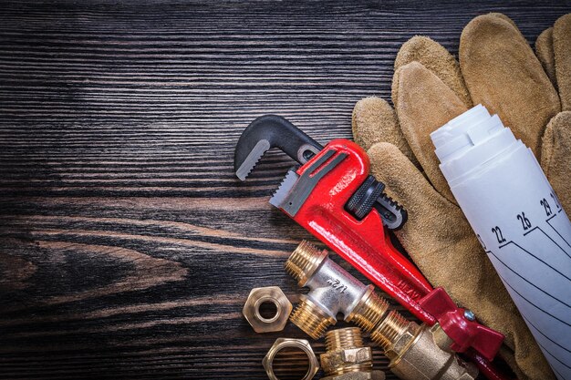 Защитные перчатки гаечный ключ чертежи сантехнических разъемов на деревянной доске.