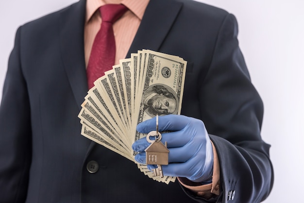 Safety sale or rent house man in medical gloves hold house key and dollar. ncov2019