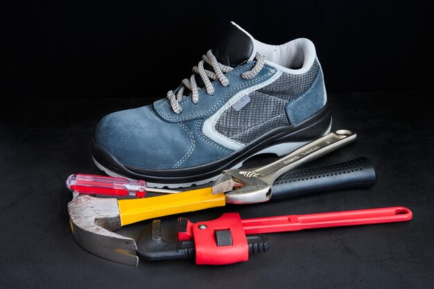 A safety shoes, hammer, screwdriver and wrenches on black\
background