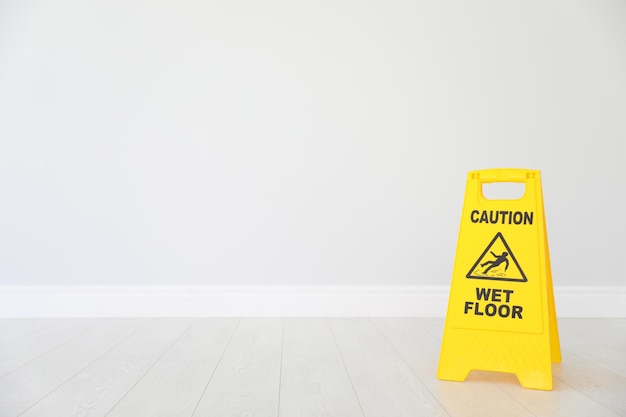 Safety sign with phrase CAUTION WET FLOOR on floor near light wall