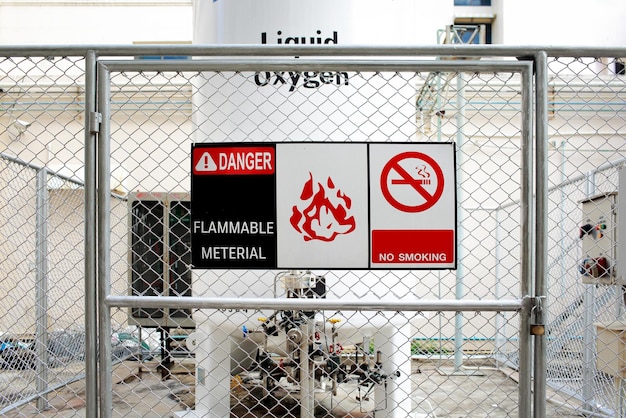 대형 액체 산소 탱크 앞의 DANGERFLAMMABLE MATERIALNO SMOKING 경고 안전 표지판