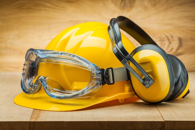 Safety of work construction safety tools yellow helmet blue goggles and earphones on wood background