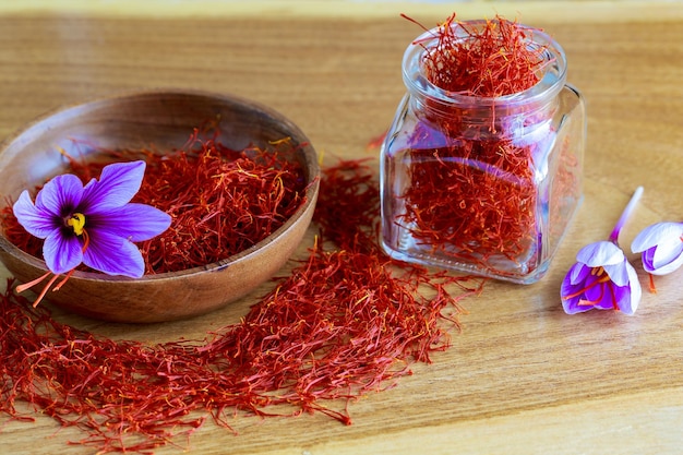 Saffron red stamens and crocuses in a wooden bowl and filled jar with stamens on a wooden table