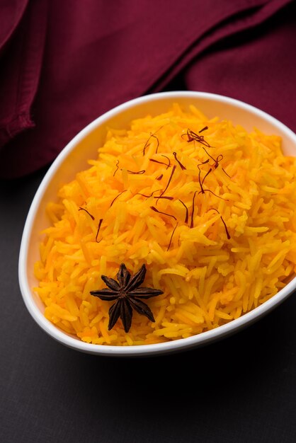 Saffron rice or Kesar chawal or bhat, served in a white ceramic bowl, selective focus