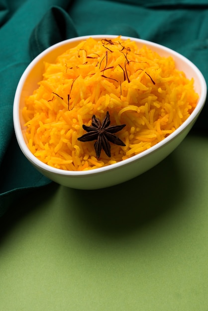 Saffron rice or Kesar chawal or bhat, served in a white ceramic bowl, selective focus