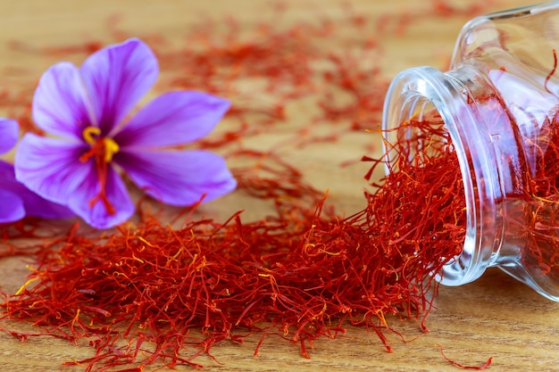 유리 병에서 나무 표면에 흩어져있는 사프란 오명. 사프란 크로커스 꽃. 사프란 sativus 꽃.
