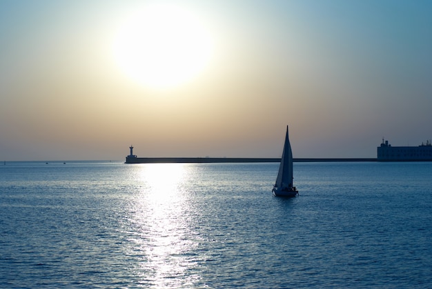 Sail boat against sea sunset. Blue marine landscape.