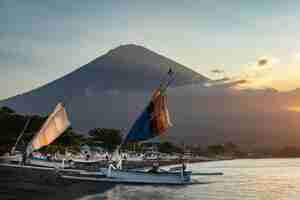 Photo sail boats at the coast of blacksand beach in amed bali and mount agung volcano in the background