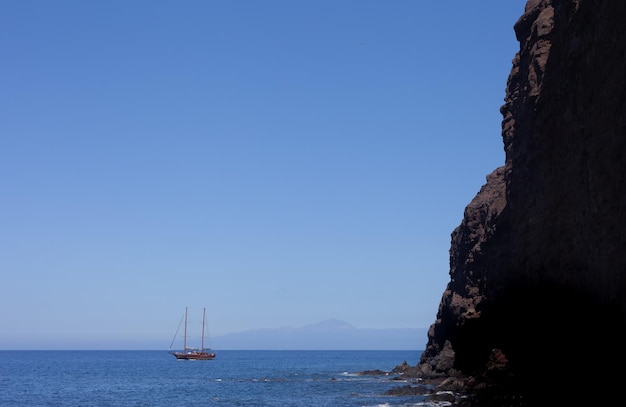 a sailboat anchored in front of a cliff on a beach on the Canary Island of Gran Canaria