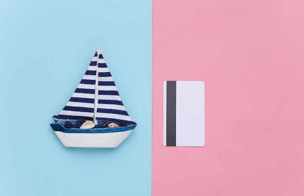 Sailboat and bank card on a blue pink background. Minimalism travel concept. Top view. Flat lay