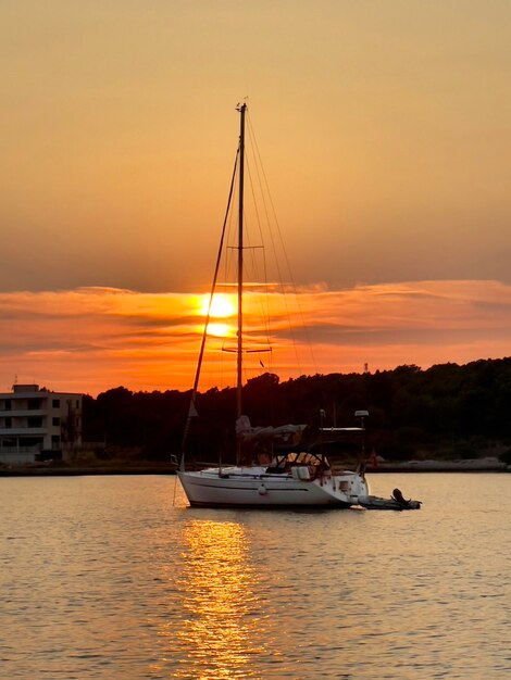 a sailboat is sailing in the water with the sun setting behind it