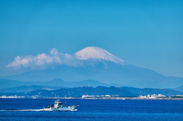 写真 空の反対側の山に沿って海を航海する帆船