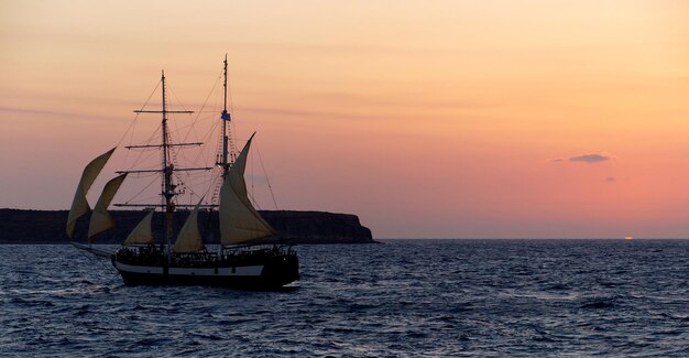 写真 夕暮れの空に向かって海を航海する帆船