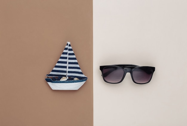 Sailboat and sunglasses on brown beige background. Travel concept. Top view