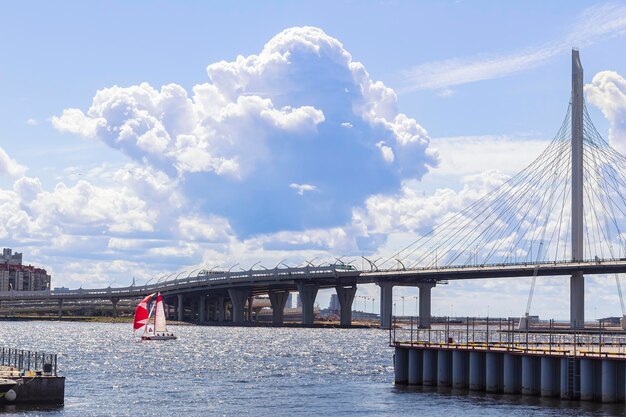 Sailboat with red sails with people on board and modern Yacht Bridge in St Petersburg on blue sky