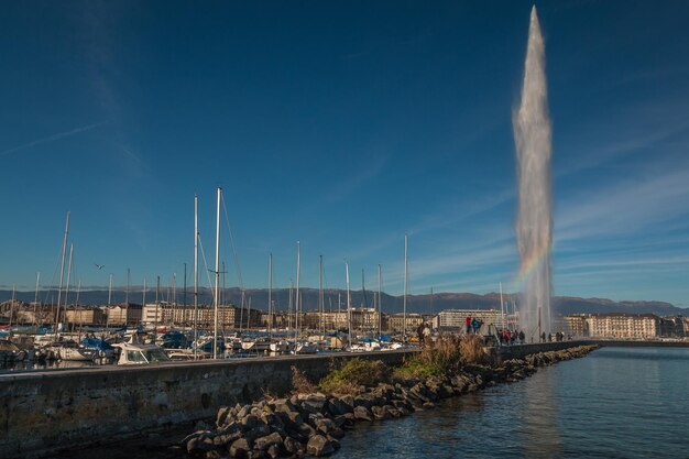 Sailboats in harbor by buildings against blue sky