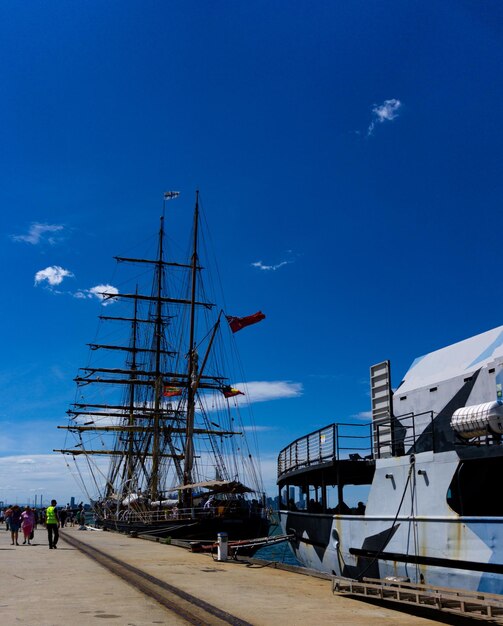 Sailboats moored at harbor against blue sky