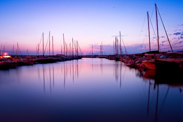 Sailboats moored in harbor at sunset