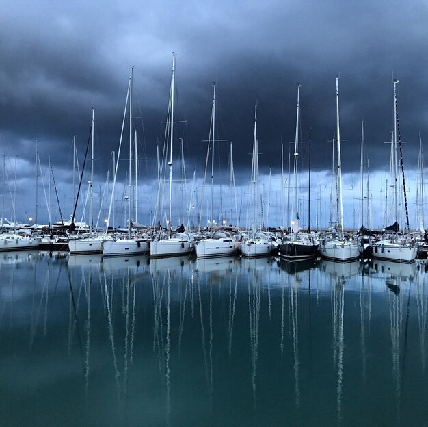sailboats moored in sea against cloudy sky