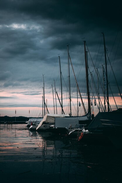 Sailboats moored in sea against sky at sunset