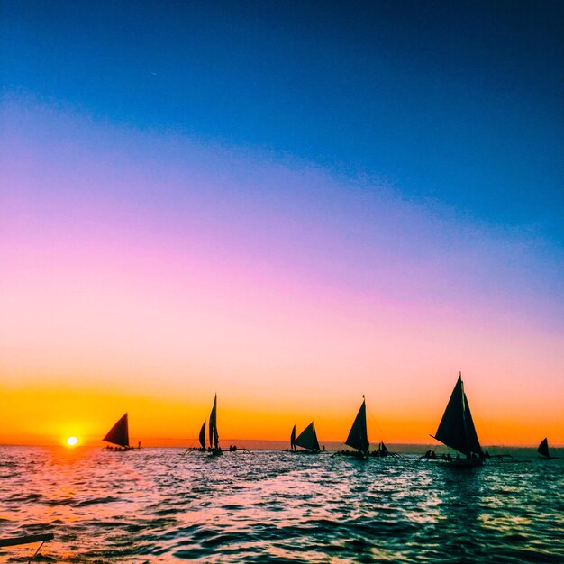 Sailboats sailing in sea against clear sky during sunset