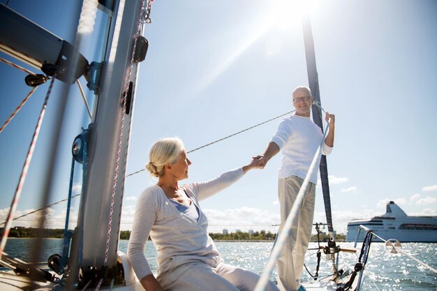 写真 セーリング、年齢、観光、旅行、人のコンセプト – 海に浮かぶ帆船やヨットのデッキで手をつないでいる幸せな老夫婦