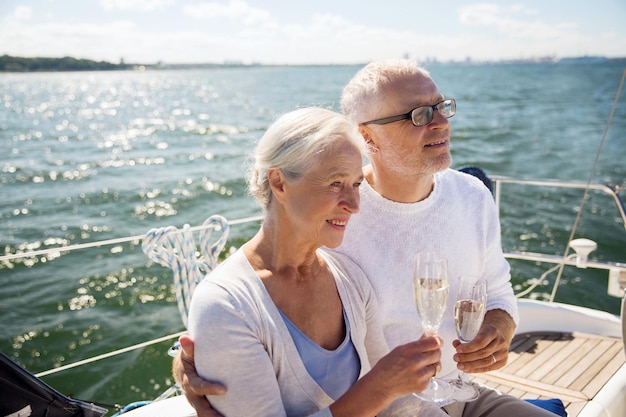 セーリング、年齢、観光、旅行、人のコンセプト – 海に浮かぶ帆船やヨットのデッキでシャンパンを飲む幸せな老夫婦