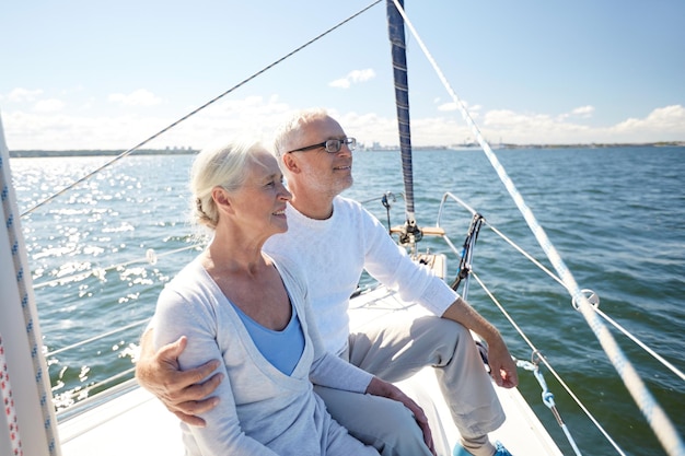 sailing, age, tourism, travel and people concept - happy senior couple hugging on sail boat or yacht deck floating in sea