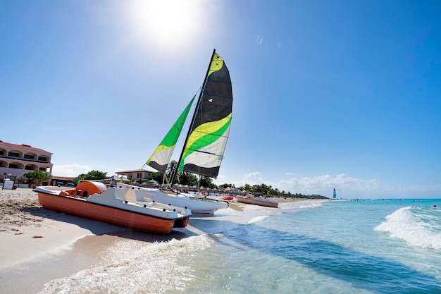항해 쌍동선은 쿠바의 아름다운 열대 자연 관광 명소를 배경으로 해변의 백사장에 주차되어 있습니다.