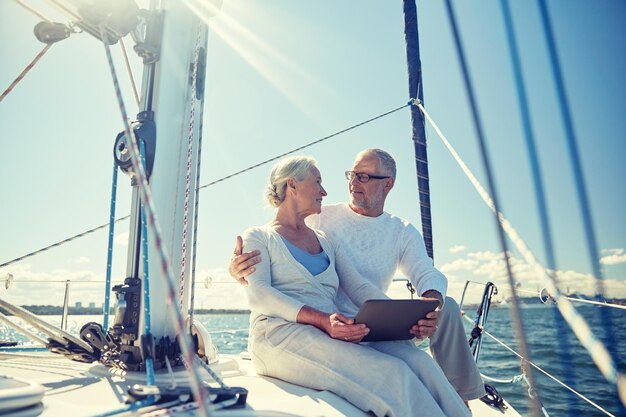 Foto navigazione, tecnologia, turismo, viaggi e persone concetto - coppia di anziani felici con tablet computer che parlano sul ponte di una barca a vela o di uno yacht che galleggia in mare