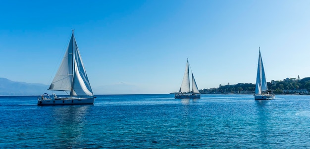 Foto barche a vela con vele bianche nel mare blu marino di belle navi nel golfo di mare con costa di montagna sullo sfondo