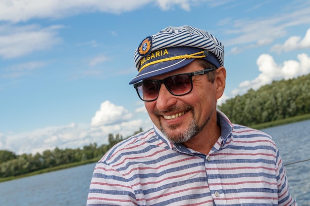 Sailor man in a cap on a boat under sail against the sky and water