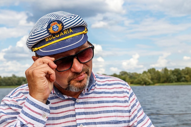 Sailor man in a cap on a boat under sail against the sky and water