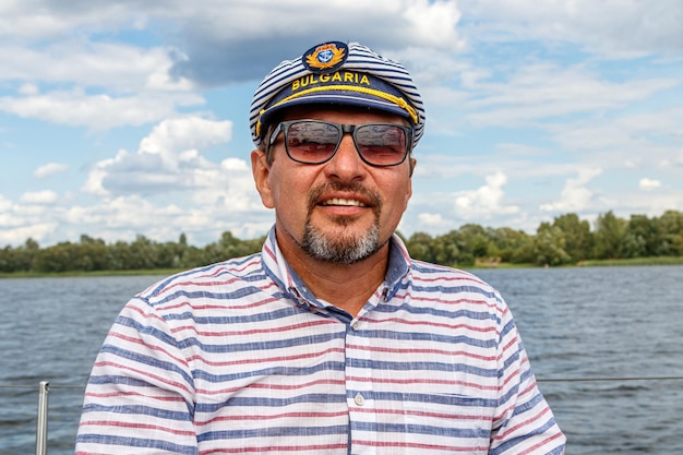 Sailor man in a cap on a boat under sail against the sky and water