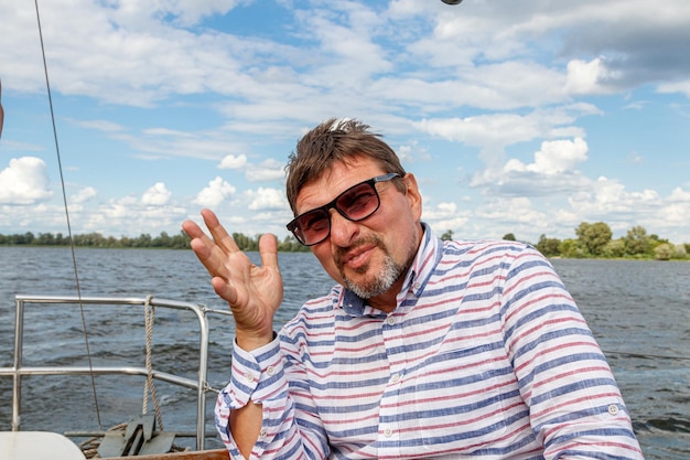 Sailor man in a cap on a boat under sail against the sky and water