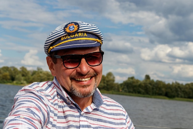 空と水に対して帆の下でボートに乗って帽子をかぶったセーラー男