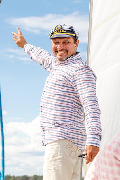 Sailor man in a cap on a boat under sail against the sky and water