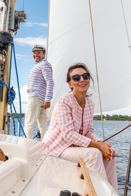 Sailor man in a cap with a girl on a boat under sail against the sky and water