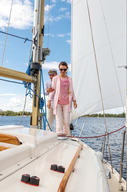 Sailor man in a cap with a girl on a boat under sail against the sky and water