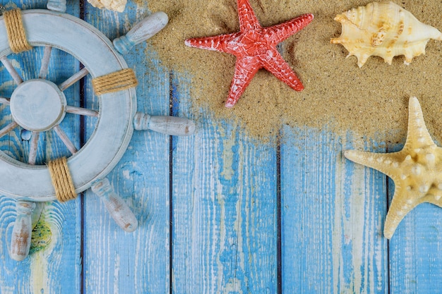 Foto ruota del capitano del marinaio con conchiglie, stelle marine, sabbia, tavole di legno blu
