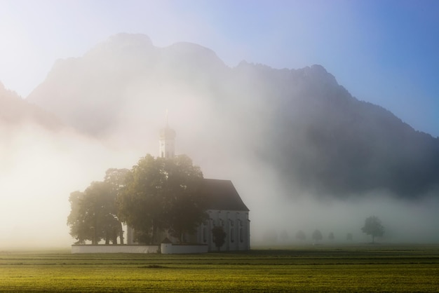 Saint Coloman kerk met warm licht schijnt door de mist in de buurt van kasteel Neuschwanstein Fussen Beieren Duitsland