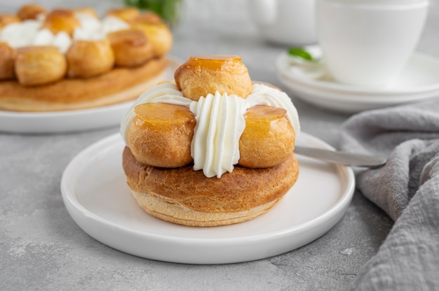 Torta di santo onore con profitrols, caramello, crema pasticcera e panna montata su un piatto.