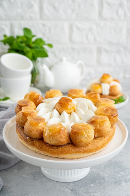 Saint Honore cake with profitrols, caramel, custard and whipped cream on a white plate on a gray concrete background. Traditional French dessert. Copy space.