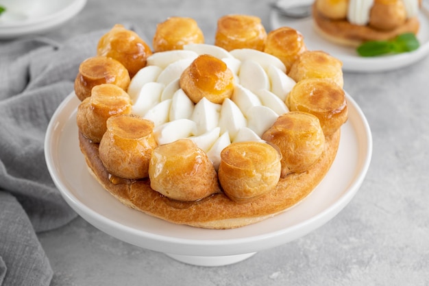 Torta di saint honoré con crema pasticcera al caramello profitrols e panna montata su un piatto bianco