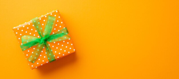 Saint Patricks Day concept Top view photo of giftbox in wrapping paper with polka dot pattern and green ribbon bow on isolated orange background with copyspace