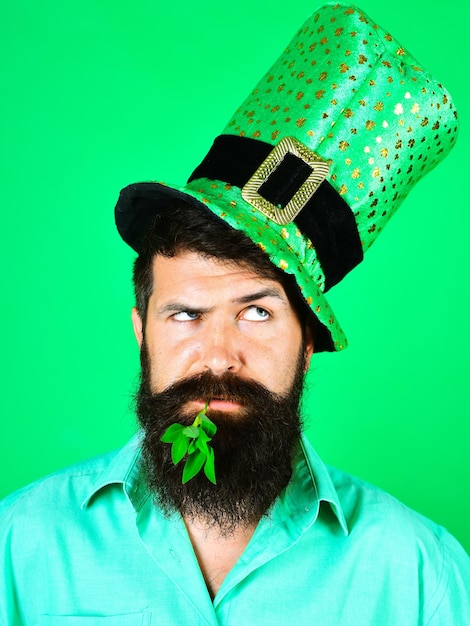 Foto uomo barbuto del giorno di san patrizio con cappello leprechaun con trifoglio in bocca uomo pensieroso in verde superiore