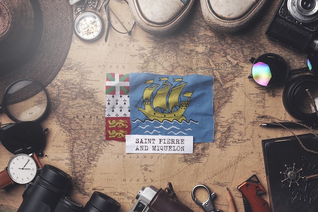 Saint Pierre and Miquelon Flag Between Traveler's Accessories on Old Vintage Map. Overhead Shot