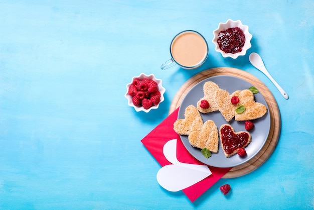 Saint valentine day achtergrond, hartvormige toast brood met frambozenjam en een kopje koffie op blauwe achtergrond