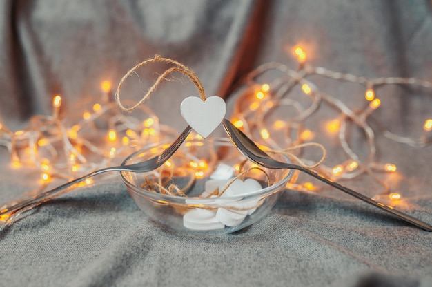 Foto carta di san valentino. cuori di legno bianchi su sfondo luminoso. cuori con luci ghirlanda. il cucchiaio e la forchetta tengono un cuore con bokeh luminoso.