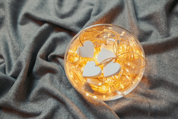 Saint Valentine's day card. White wooden hearts with garland lights in the bowl on the gray background. Plate with hearts and lights.